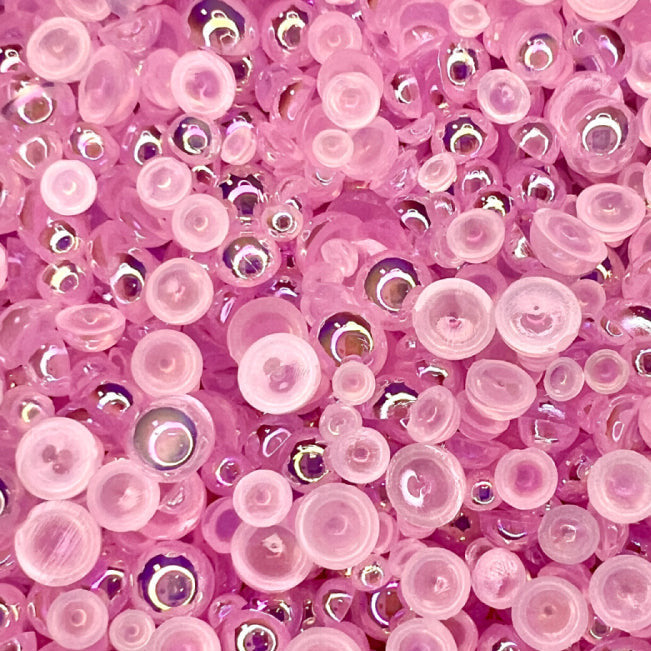 A close-up image of flat-back transparent iridescent pale pink acrylic pearls used as embellishments.